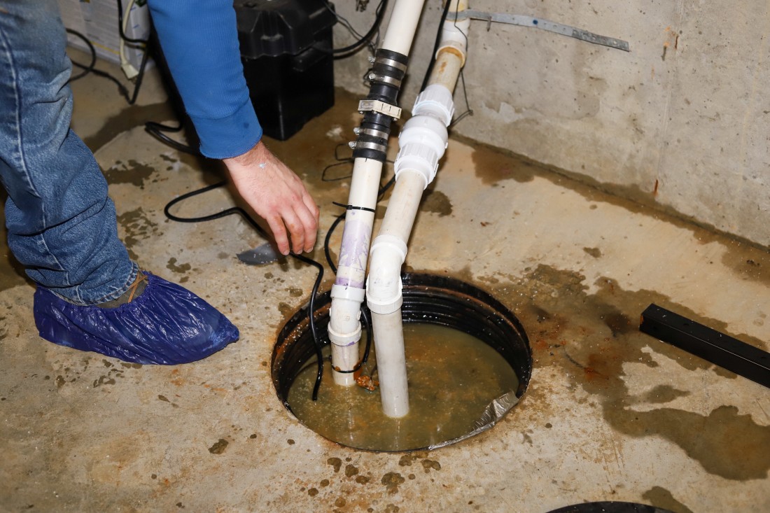 worker working to fix a sump pump failure in a basement