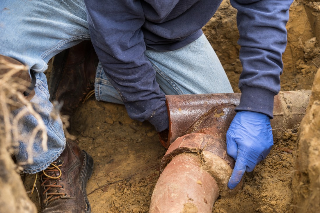 man holding a pipe trying to fix a sewer backup