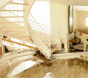 Content damage of a white staircase on the left and piano on the right with different items all over the floor