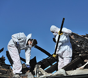 workers in white hazmat suits working on destroyed property